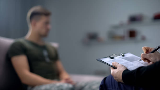 心理学者は悲しい男性兵士、ptsdとの��セラピーセッション中にメモを作る - military man ストックフォトと画像