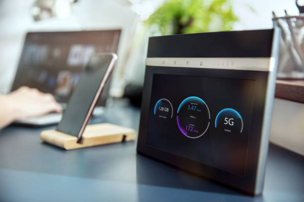 Modern 5G wi-fi router with display on the desk and devices on the background. Interface on the screen was created in graphic program. stock photo