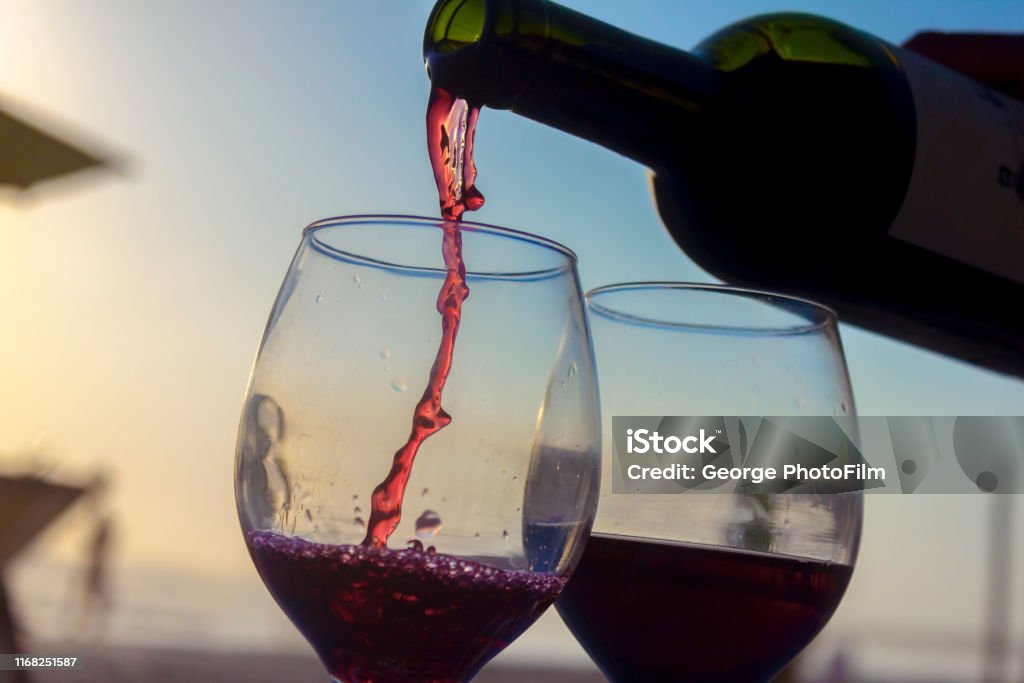Liquid of wine on the sunset beach Activities on the sunset. bottle of wine serving wine on two cups on the beach Wine Stock Photo