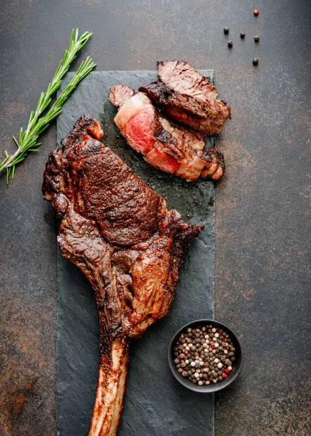 Top view of grilled beef steak Tomahawk with spices on a black slate. Flat lay, dinner concept.