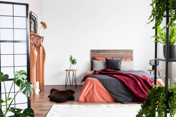 istock Copy space on empty white wall of rustic bedroom interior with king size bed with orange bedding and burgundy blanket 1168253219