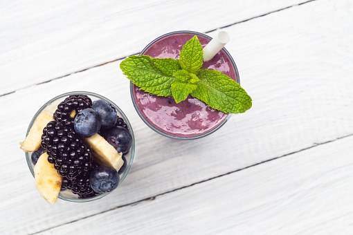 Smoothies of banana, blueberry, blackberry, oatmeal and yogurt and ingredients in two glasses on a white table. Top view