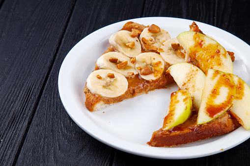 Close up view on breakfast sweet toast with banana and apple poured with caramel on dark background with copy space. Sandwich meal. Food for breakfast.
