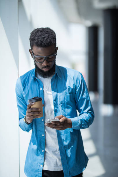 istock Businessman with cup of tea use smartphone while standing by office window 1168257401