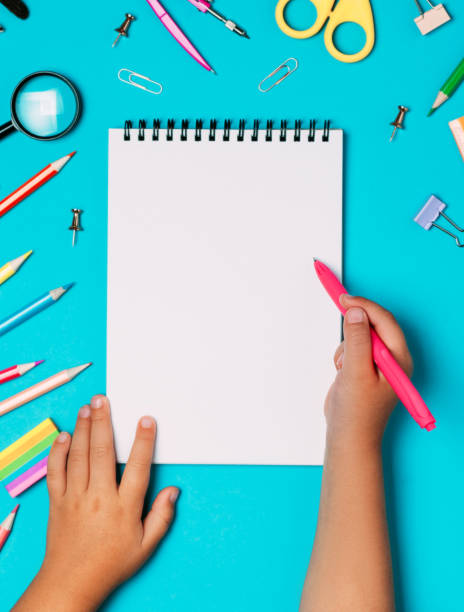 istock School supplies and stationery with children hand writing in empty notebook on blue table top view. 1168258659