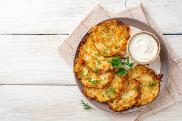 potato pancakes or latkes or draniki with sour cream in plate on white wooden table - latke imagens e fotografias de stock