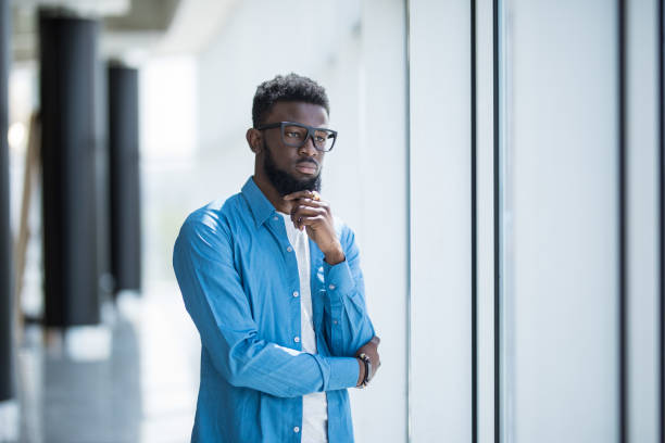 istock Young African in glasses designer looking through window thinking about the future 1168259601