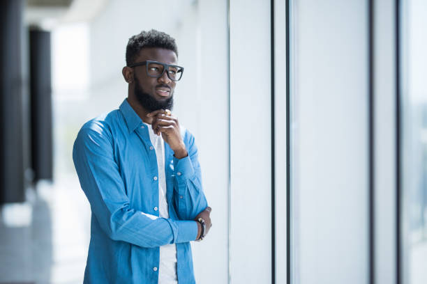 istock Young African in glasses designer looking through window thinking about the future 1168259695