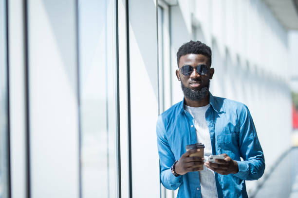 istock Young african-american businessman use mobile phone near panoramic windows in office while drink coffee 1168259761