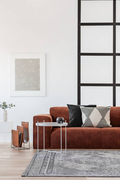 elegante divano ad angolo marrone con cuscini a motivi geometrici in eleganti interni del soggiorno con pareti di montanti - mullions foto e immagini stock