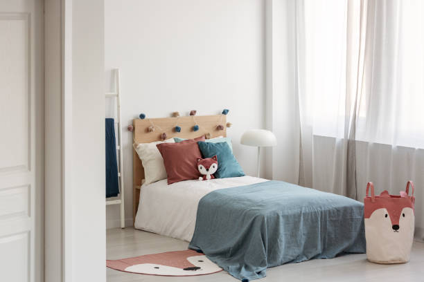 istock Bright bedroom interior with single bed with turquoise blanket on white bedding and colorful pillows and toy 1168260927