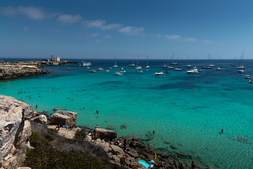 Favignana, Italy - August 09, 2019: The famous Cala Azzurra beach in the beautiful island Favignana in Sicily, during a sunny summer day. People are relaxing and enjoying the day