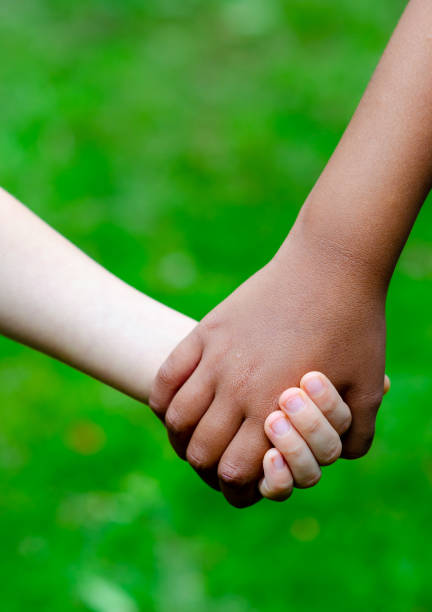Boy and girl of different races hold hands together. Boy is Caucasian (white skin) and the girl has black skin (dark). stock photo