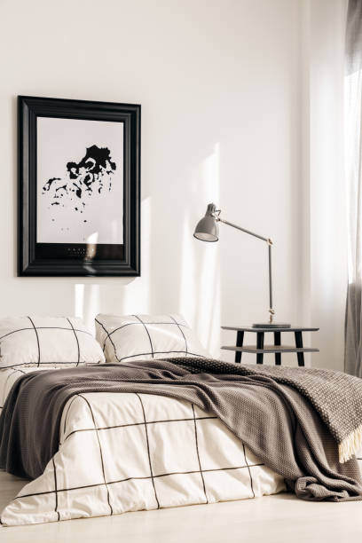 istock Industrial lamp on nightstand table next to king size bed in white bedroom interior 1168267362