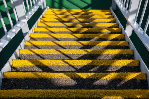 Looking down the external deck steps, that connect lower and upper decks on a ferry Looking down the external deck steps, that connect lower and upper decks on a commercial ferry. Each step is painted bright yellow so are clear to see for passengers going up and down the stairway. The texture of the steps is rough, which gives better grip in all weather. Shadows from the sunny day are creating interesting patterns across the stairway. White painted railings run down each side, leading down to the green deck area. oban stock pictures, royalty-free photos & images