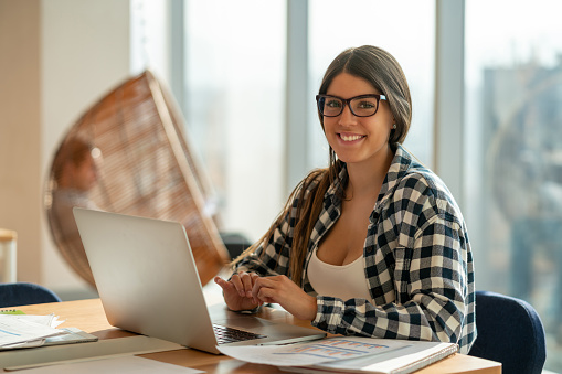 Young woman at a coworking office working with a laptop and looking at camera very cheerfully and smiling