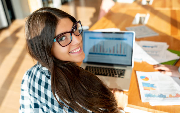 istock Beutiful young woman wearing eyeglasses facing camera smiling while working on laptop at the office 1168290488