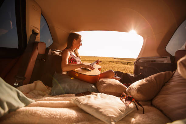 istock Young woman relaxing on her camping trip while playing guitar and watching sunset 1168294347