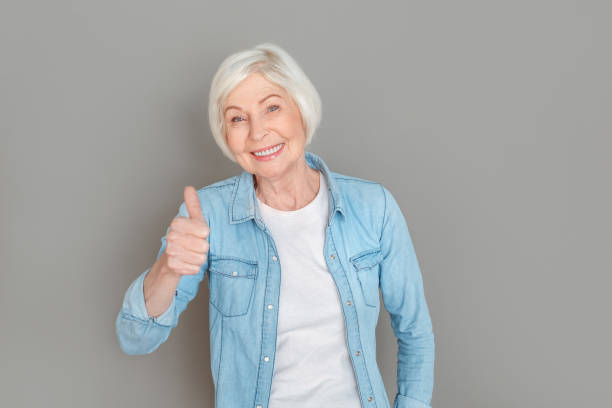 istock Senior woman in jeans jacket studio isolated on grey wall thumb up 1168294400