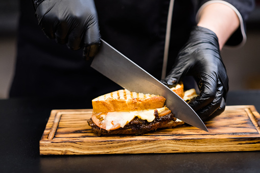 Grill restaurant. Cropped shot of chef using knife to cut smoked turkey breast sandwich on wooden board.