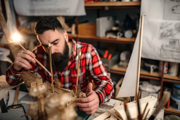 Bearded man making sailboat in his garage for hobby