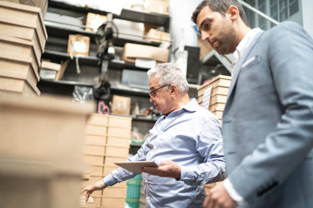 istock Senior and young business owner checking products in a storage room, using digital tablet 1168298590
