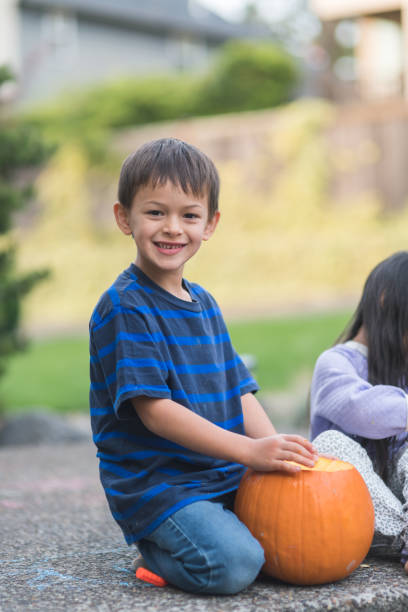 A young boy smiles at the camera while he carves a pumpkin on the patio.