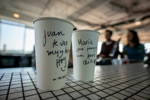 Close up of take out coffee cups with messages for each customer at a cafeteria - Focus on foreground