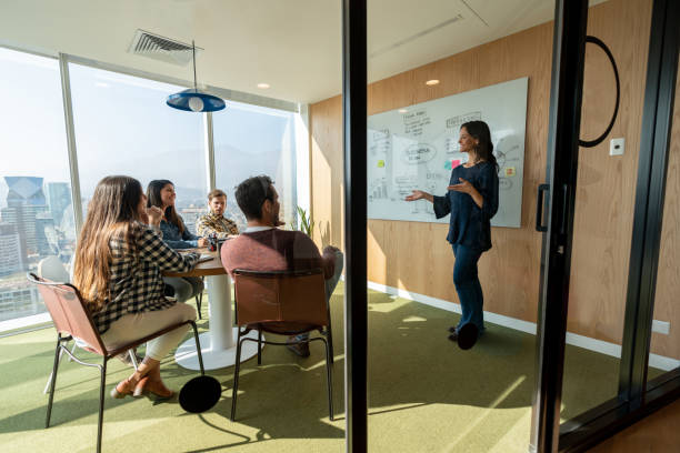 istock Latin american woman training her team during a meeting addressing them using a white board at the office 1168307549