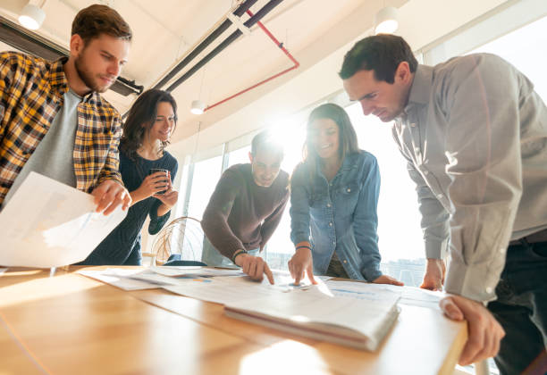 istock Group of young business people in a meeting pointing at a document on table while discussing business 1168308161