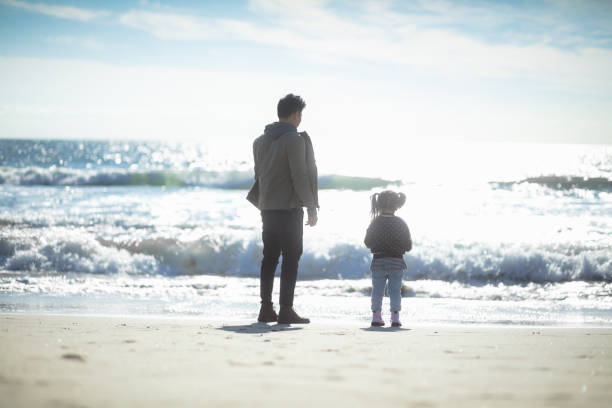 istock Father and Daughter Looking Out at Ocean Waves 1168309108