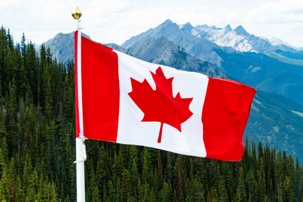 istock Canadian Maple Leaf national Flag flying over mountains 1168310157