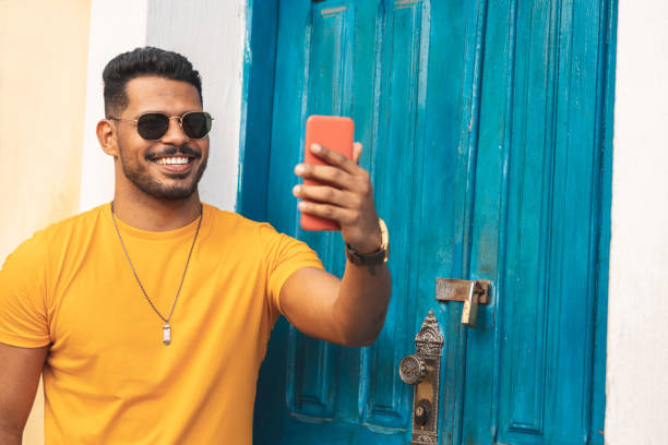 latinoamericano tomando un selfie frente a la puerta azul - men latin american and hispanic ethnicity young men smiling fotografías e imágenes de stock