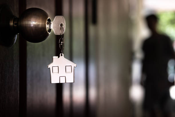 Home key with house keyring on wooden door with unknown blur visitor shadow background stock photo