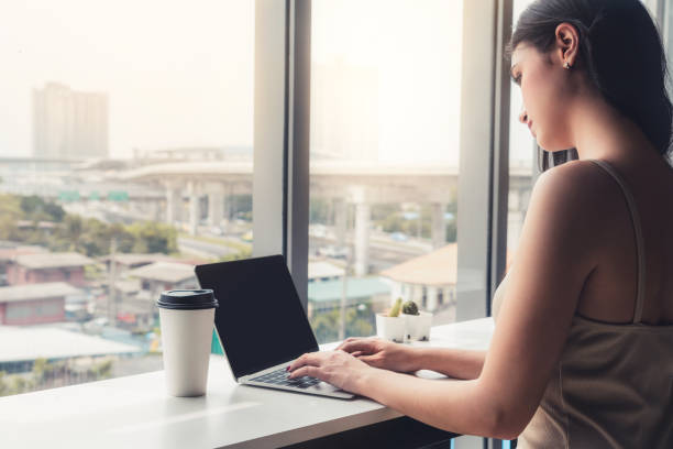 istock Young business woman using laptop computer while sitting at cafe table next to office windows. 1168319505