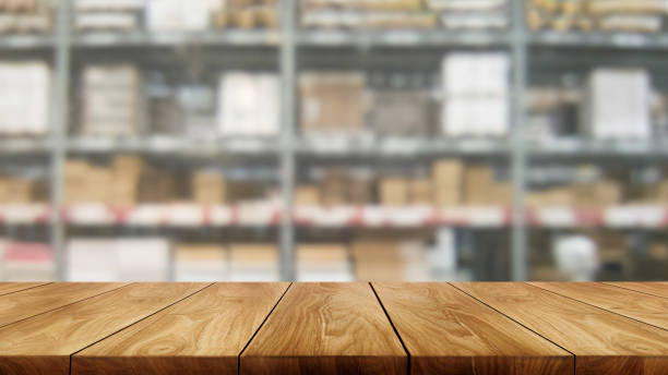 Wood table in warehouse storage blur background with empty copy space on the table for product display mockup. Hardware goods distribution and industrial logistics concept.
