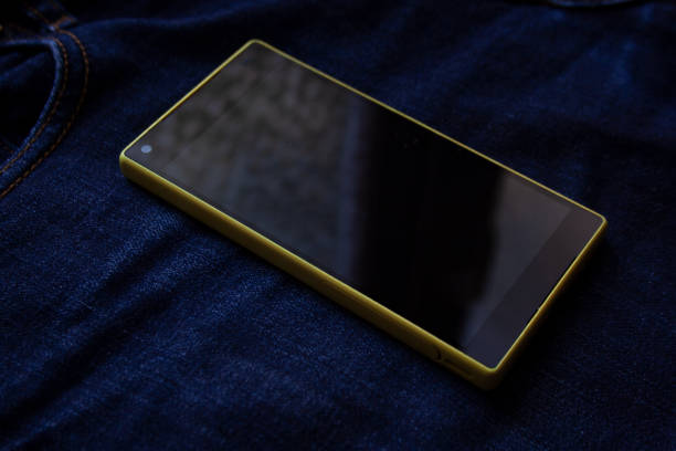 Modern smartphone with bright yellow bezels on dark blue jeans