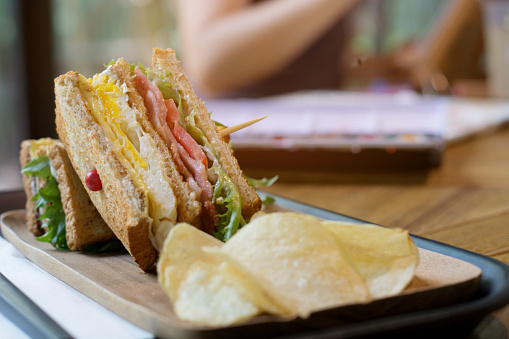 Selective focus of club sandwich with bacon - chicken, fie egg, cheese, potato and lettuce on wooden tabel in cafe background.