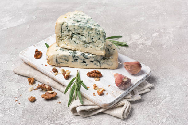 Tasty soft blue cheese with spices of rosemary and garlic Tasty soft blue cheese with spices of rosemary and garlic on white wooden board and gray concrete background roquefort cheese stock pictures, royalty-free photos & images