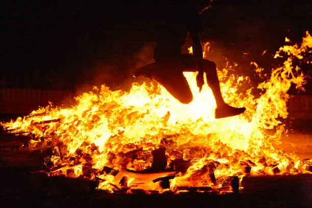 Photo of Summer solstice celebration in Spain. Woman jump. Fire flames