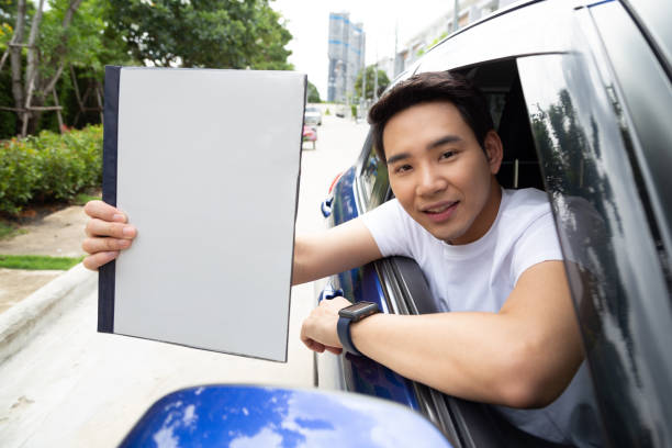 jeune homme asiatique retenant le livre de voiture de police et s'asseyant dans la voiture, concept personnel d'assurance d'accident - car loan audio photos et images de collection