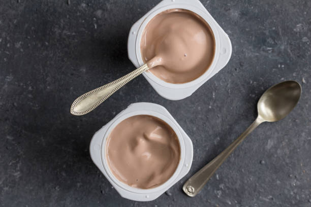 istock Two chocolate flavoured yogurts in plastic cups with spoons on grey texture background 1168339589