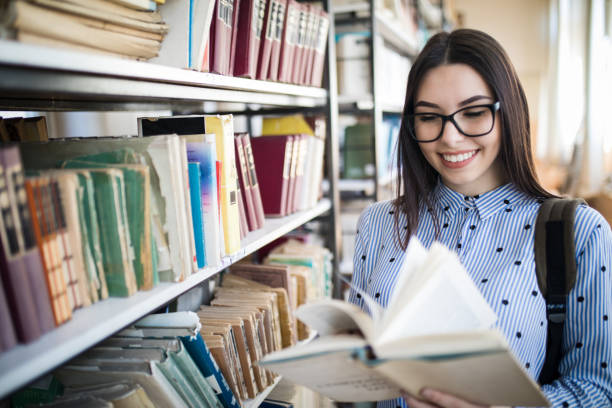istock Young student with books and backpack standing by bookshelf in college library 1168339956