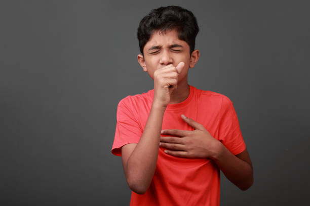 Boy coughs by closing his mouth by hands stock photo