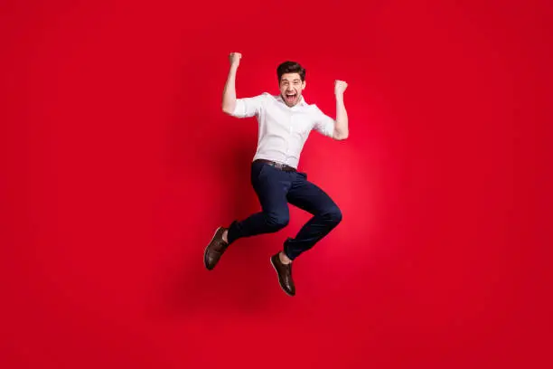 Full length body size photo of man, jumping with happiness dressed formally while isolated with red background