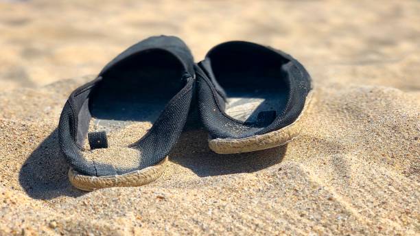 istock Pair of black espadrilles lying on the sand 1168355409