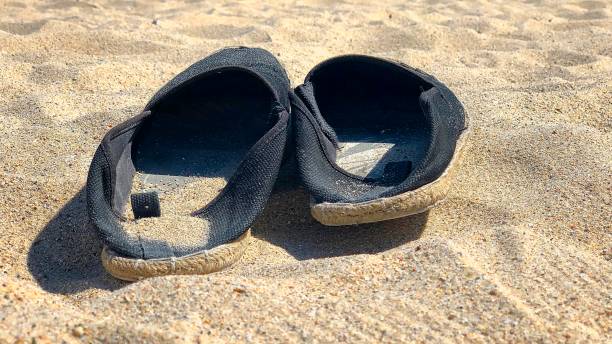 istock Pair of black espadrilles lying on the sand 1168355410