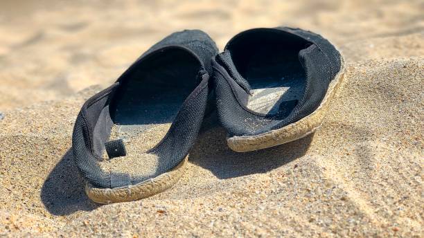 istock Pair of black espadrilles lying on the sand 1168355411