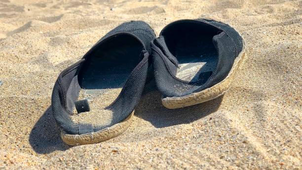 istock Pair of black espadrilles lying on the sand 1168355413