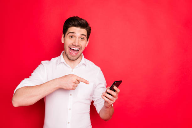 istock Copyspace photo of rejoicing man who points at his telephone laughing while isolated with red background 1168355507